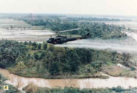 Helikopter Huey Angkatan Darat AS menyemprotkan Agen Oranye di atas lahan pertanian selama Perang Vietnam dalam kampanye perang herbisida